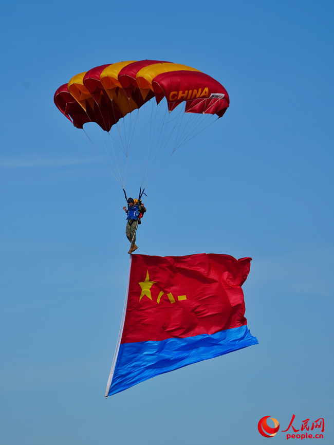 “八一”“藍鷹”跳傘隊攜帶黨旗、國旗、八一軍旗和空軍軍旗先后躍出機艙，而后，多名跳傘