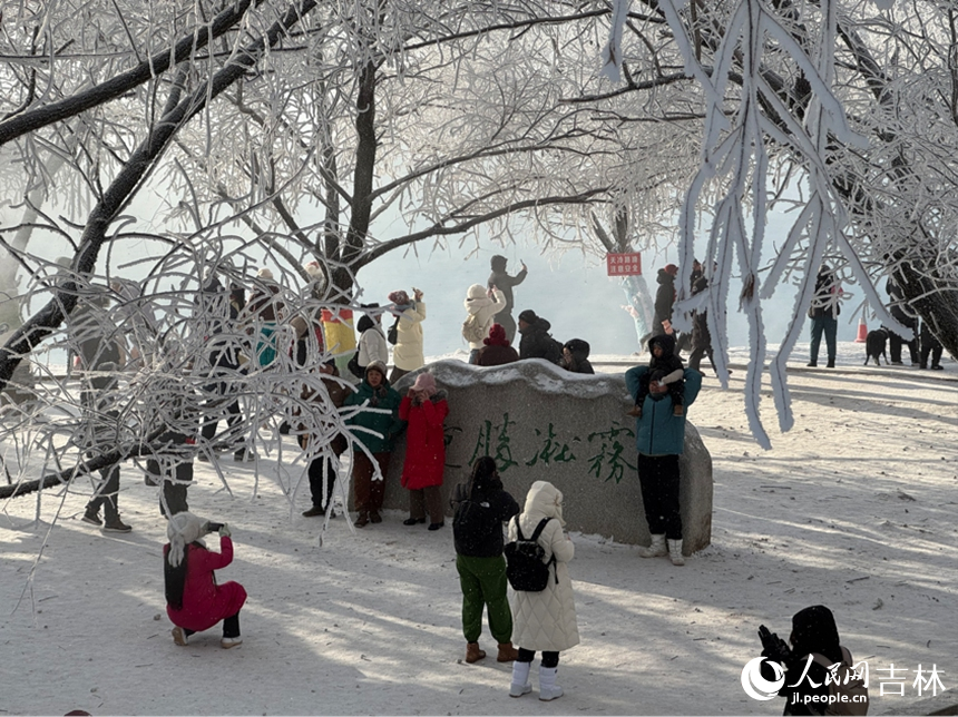 游客們聚集在刻有“霧凇勝景”的字樣的石頭前合影。人民網記者 李思玥攝